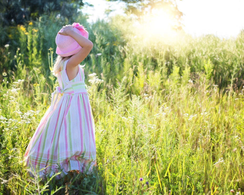 Girl in a dress and hat in a field of wild flowers.