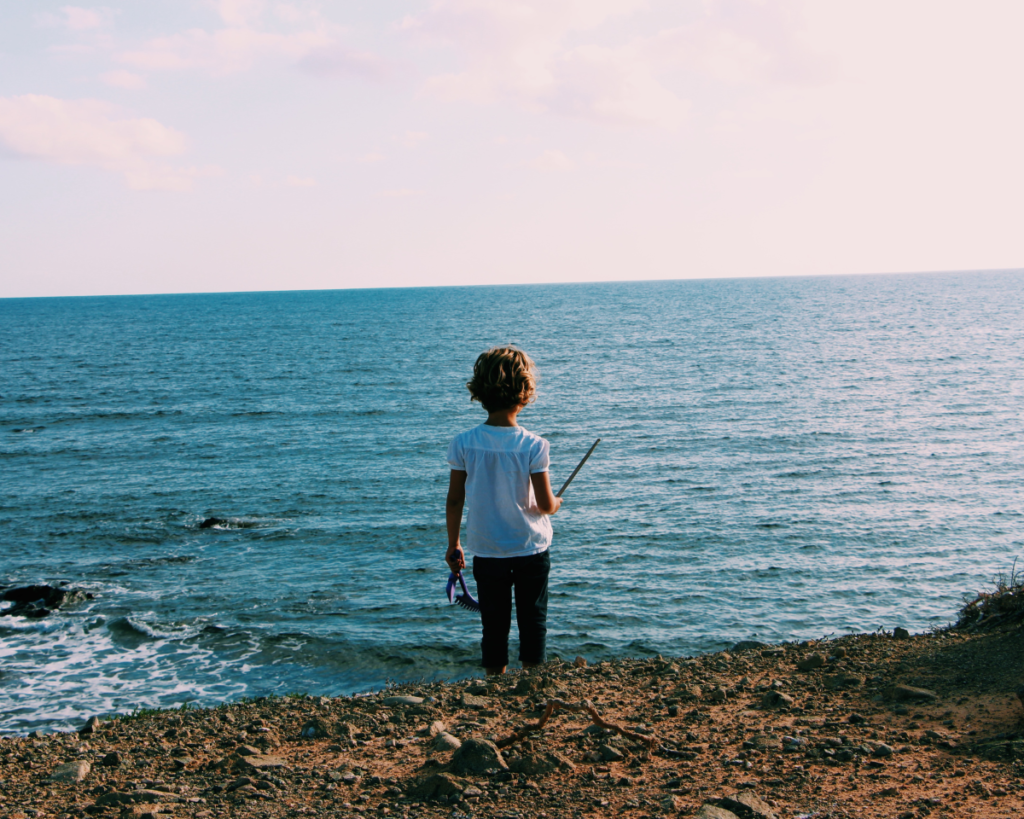 Child standing on the beach looking at the water.