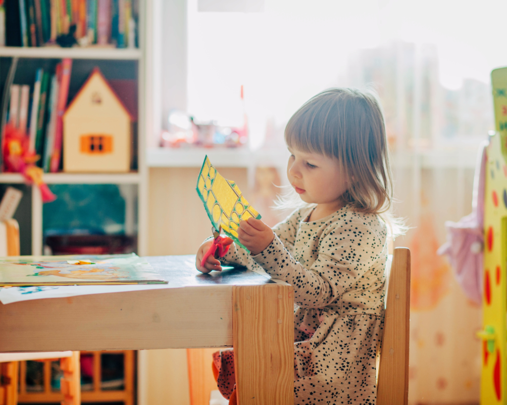 Child using scissors to cut at a child sized table.