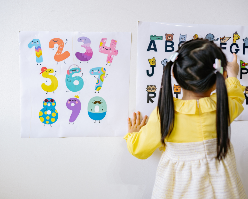 Girl with pigtails pointing to letters on an alphabet poster.