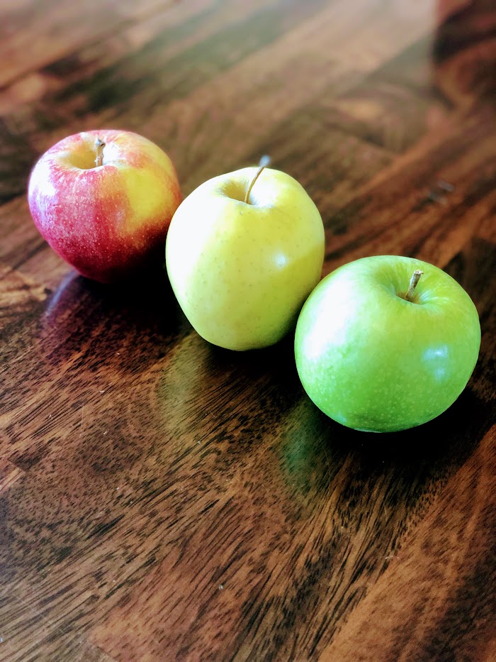 Row of red, yellow, and green apples on a wooden surface.