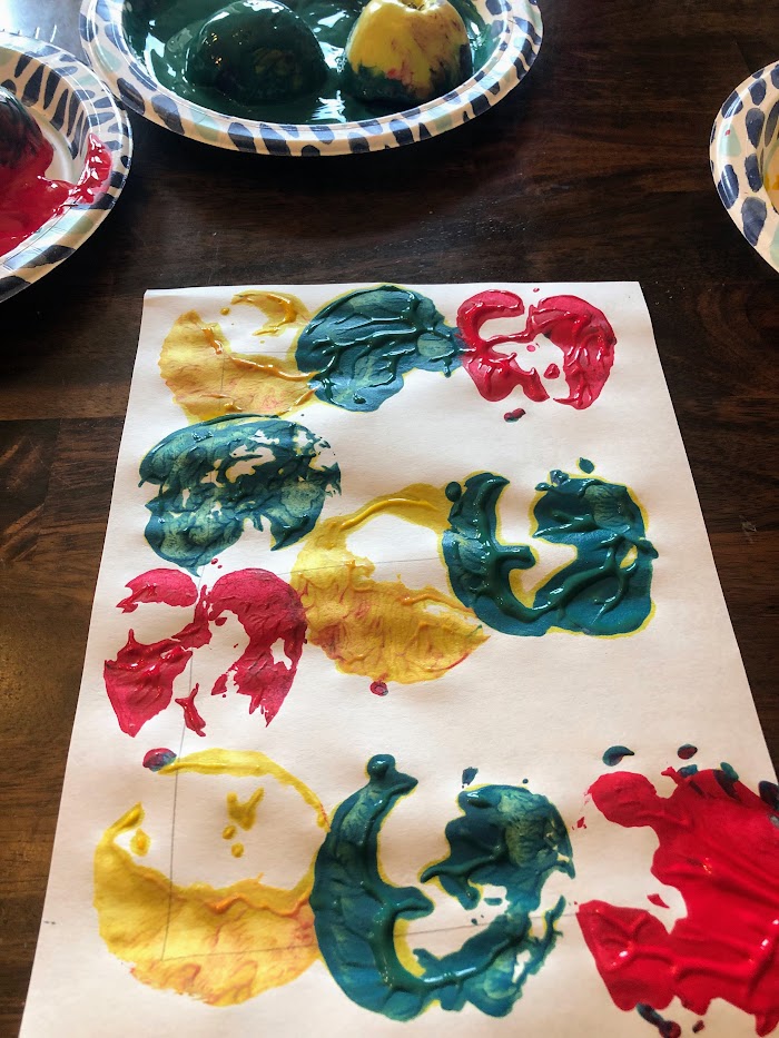 Paper with red, green, and yellow paint stamped from apples into a letter E.