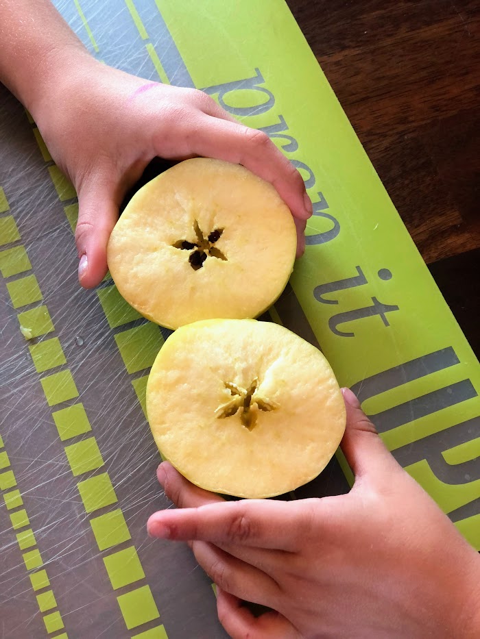 Children's hands each holding an apple half showing the seeds in the shape of a star.