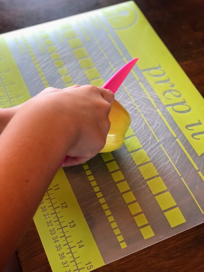 Child's hands using a plastic safety knife to cut a yellow apple in half.