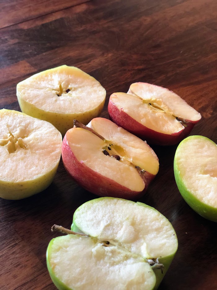 Halved yellow, red, and green apples on a wooden table.