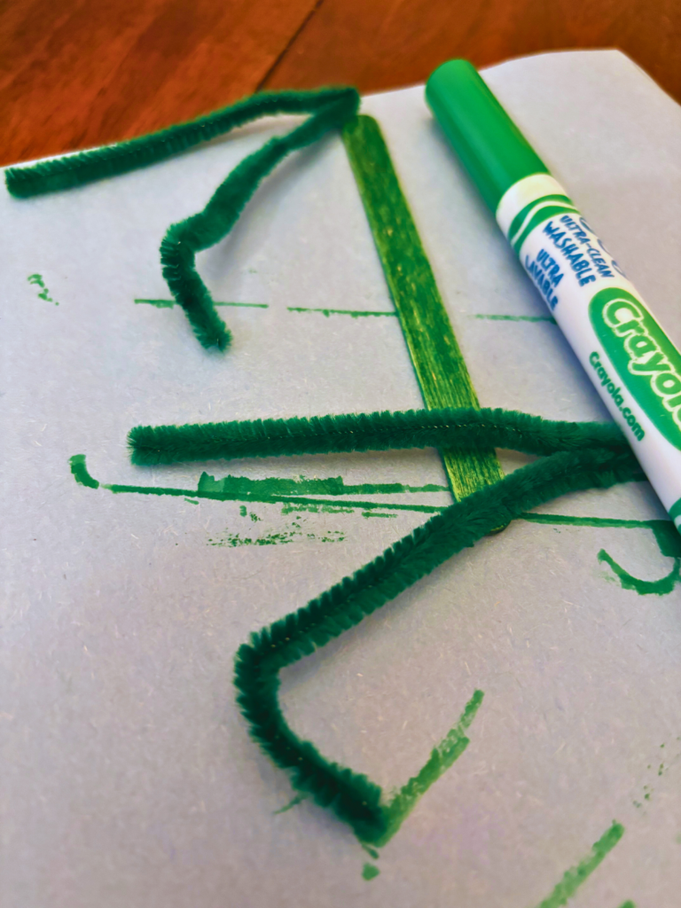 green pipe cleaners, colored green popsicle stick, and green marker on white paper