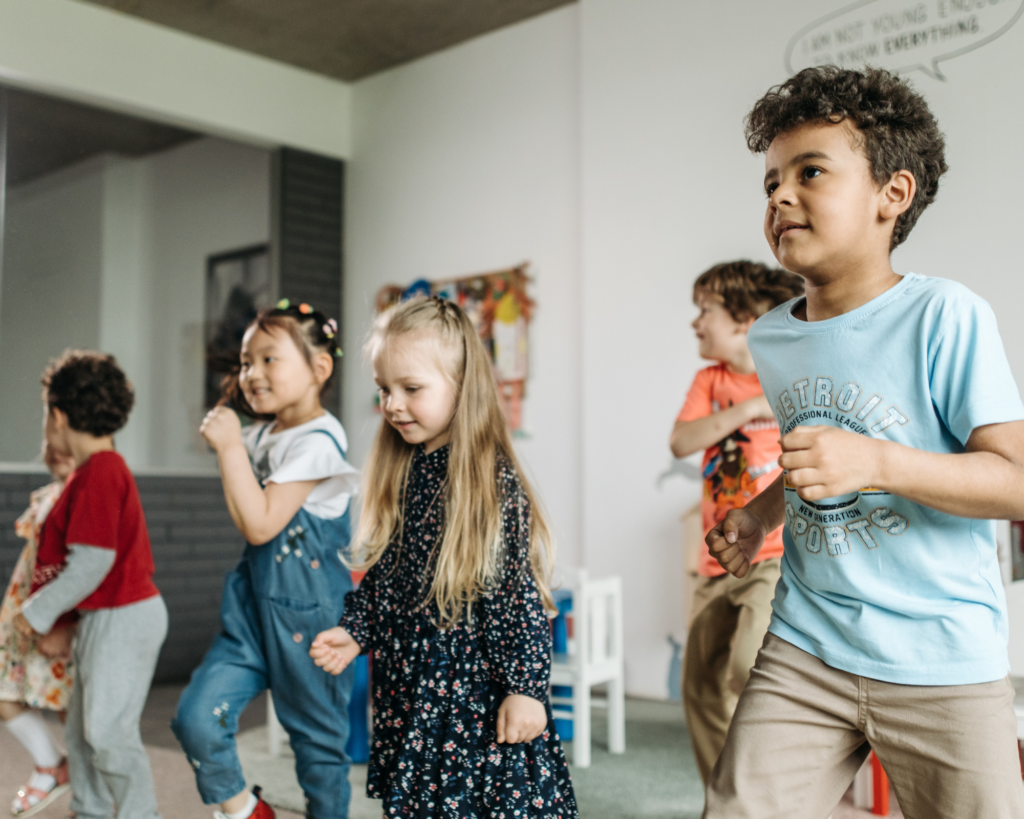 A group of preschool children singing and dancing in a classroom.