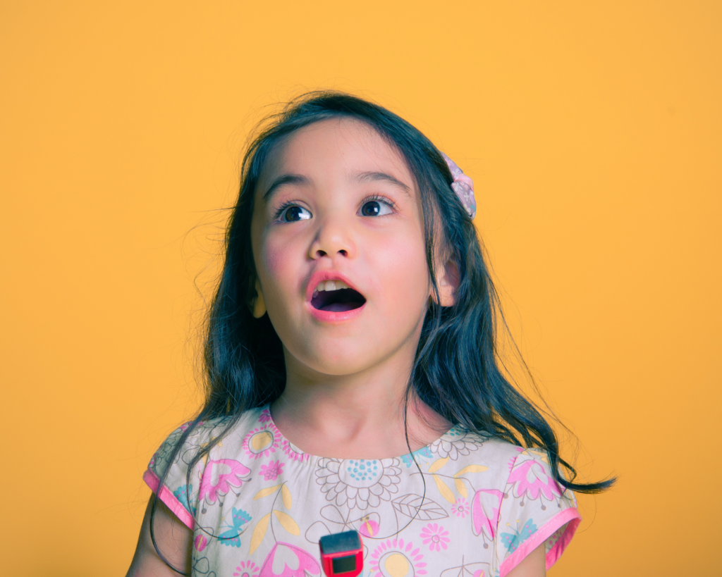 Preschool age child singing. Orange background.