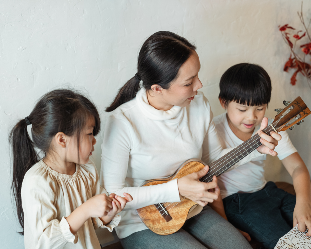 Mother playing a ukelele with her son and daughter on either side of her.