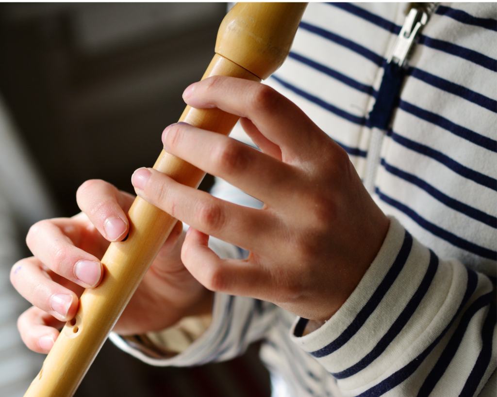 A close-up of a preschooler's hands playing a wooden recorder.