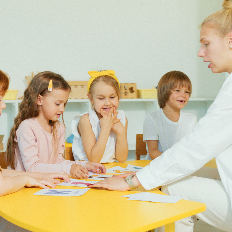 Teacher sitting at a yellow small group table doing an activity with letter cards with a group of students.